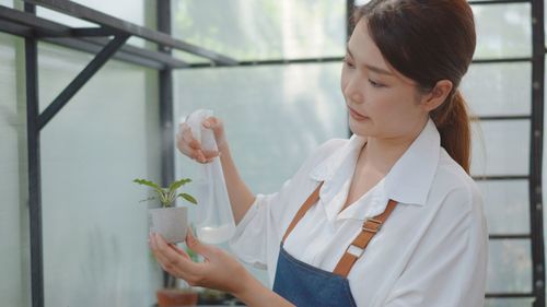 Young woman looking away while standing on potted plant