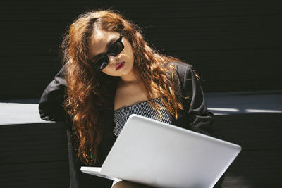 Beautiful young woman using mobile phone while sitting outdoors