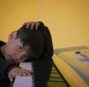 Portrait of boy leaning on piano against yellow wall