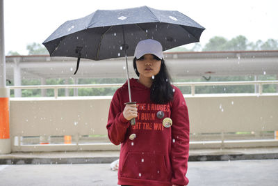 Young woman holding umbrella while standing on road during rainfall in city