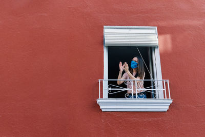 Woman sitting on window against wall