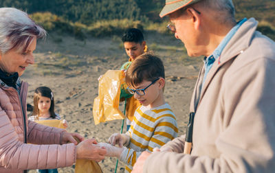 Woman assisting boy wearing gloves while cleaning beach