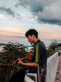 Side view of young man sitting on rock looking at view