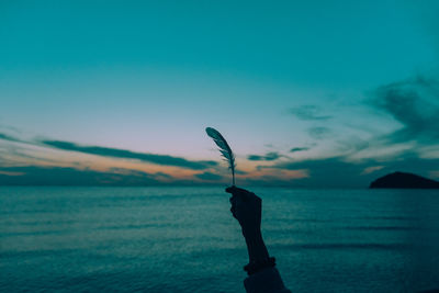 Close-up of hand against sea at sunset