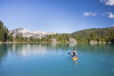 Active woman paddles stand up paddle board on blue lake.