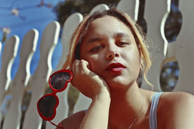 Close-up portrait of young woman holding sunglasses