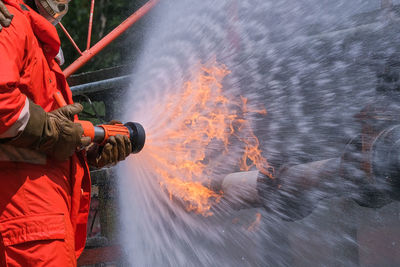 Midsection of firefighter spraying water