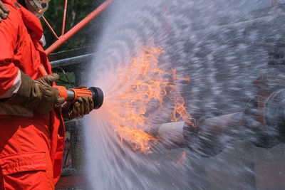 Midsection of firefighter spraying water