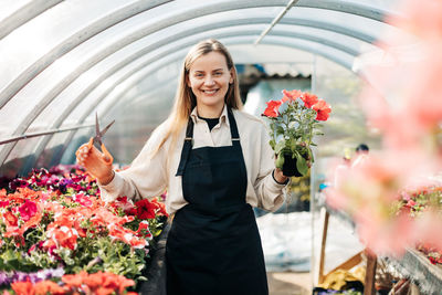 A smiling female gardener with scissors works with petunias in a greenhouse. plant care