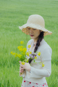 Portrait of young woman standing by flowering plants on field