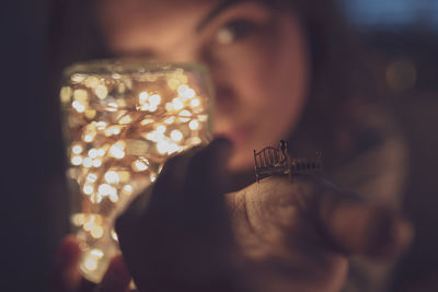 Close-up portrait of woman holding illuminated lighting equipment and miniature toy