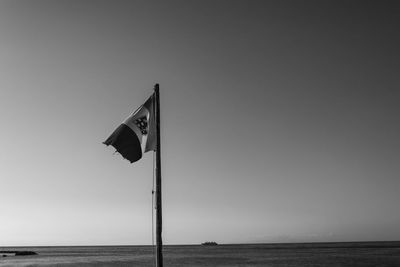 Flag sign by sea against clear sky