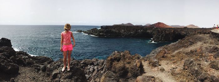 Woman standing on rock at beach against sky