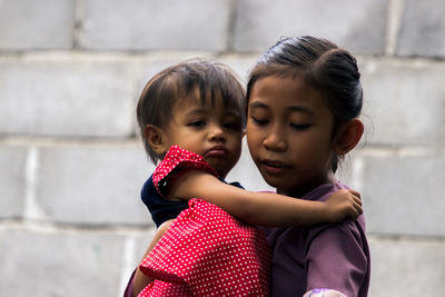 Girl carrying sister while standing against wall