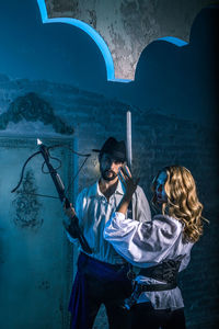 Young man holding woman standing against wall