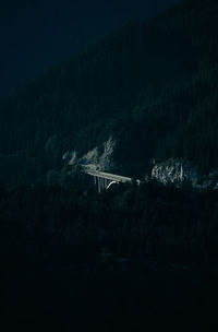 Illuminated bridge by trees against mountain during sunset