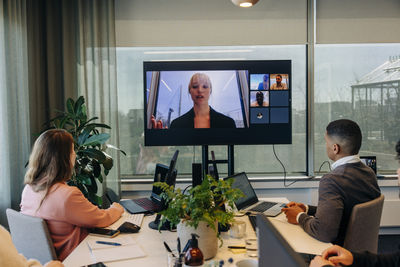 Colleagues doing video conference with businesswoman over tv screen at office