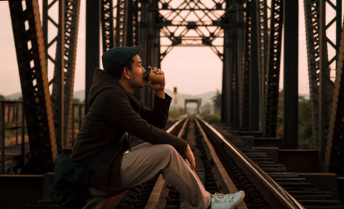 Side view of young man sitting on railroad track