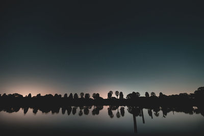 Reflection of silhouette trees in lake against sky