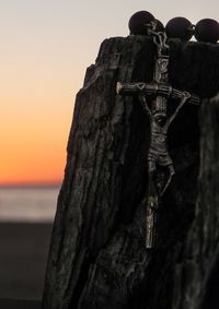 Close-up of cross against sea at sunset