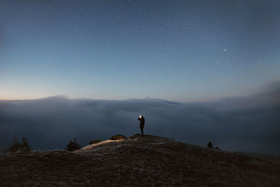 Rear view of man standing on land against sky at night