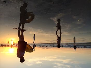 Man with inflatable ring wading in sea against sky during sunset