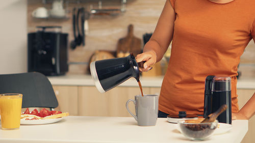 Woman pouring coffee in cup at home