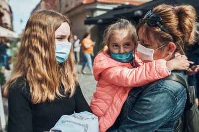 Family mother and her daughters standing in a street downtown wearing the face masks