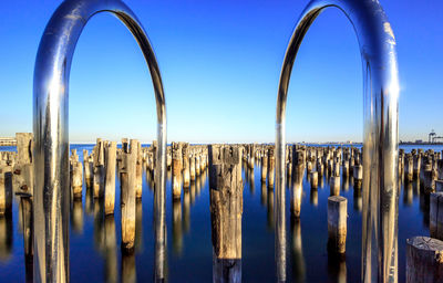 Railing against wooden posts in sea against clear sky