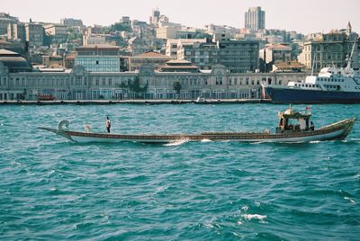 Traditional boat sailing in river against cityscape