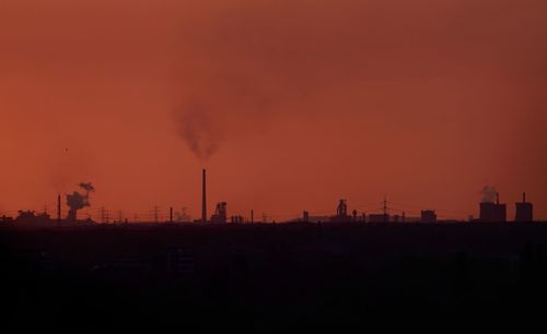 Smoke emitting from factory against orange sky