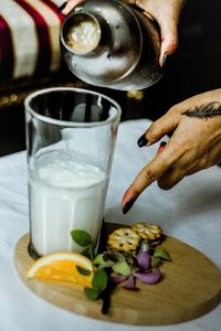 Close-up of woman hand pointing while pouring milk in glass on table 