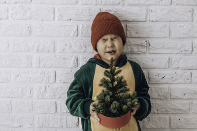 Little boy with a christmas tree in his hands squeezed his eyes shut making a wish for christmas