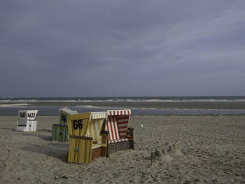 Hooded chairs on beach against sky