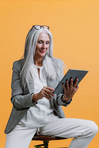 Young woman using mobile phone while sitting against yellow background