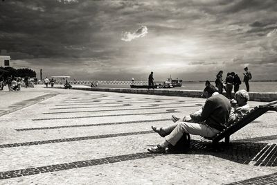 People sitting on bench against sky