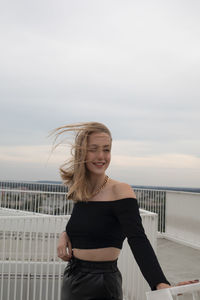 Young woman standing by railing against sky