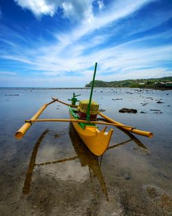 Yellow boat moored at beach against sky