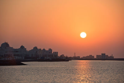 Sea by buildings against sky during sunset