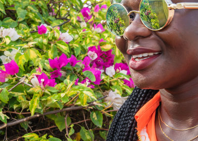 Close-up portrait of smiling young woman wearing sunglasses against plants