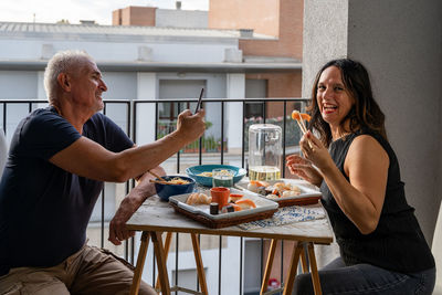 Smiling friends using mobile phone while sitting on table