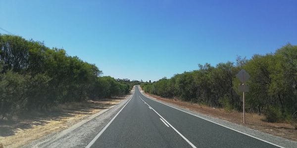 Empty road amidst trees against clear sky