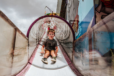 Portrait of bored boy sliding down a large slide at county fair