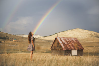 Young woman looking at rainbow standing in meadow