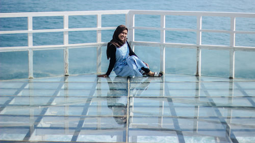 Portrait of smiling woman sitting by railing against sea