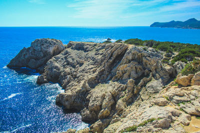 Rocks on shore by sea against blue sky