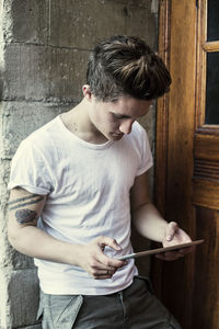 Young man using digital tablet while leaning on high school wall