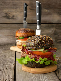 Cheeseburger with black bun, meat and vegetables on a wooden background, fast food and knife
