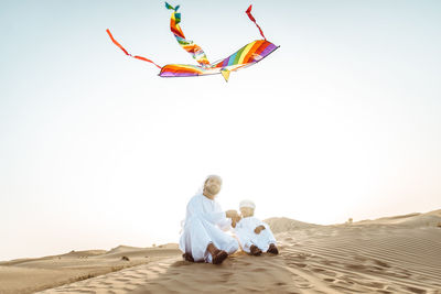 Rear view of friends sitting on land against clear sky