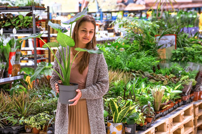 Young woman holding a pot with monstera in the middle of a flower store.